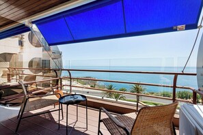 Ein Balkon mit Korbstühlen, einem kleinen Tisch und Blick aufs Meer.