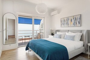Ein Schlafzimmer mit einem großen Bett, Meerblick durch eine Schiebetür, einer Deckenleuchte und einem Bild an der Wand.