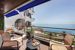 Ein Balkon mit Korbmöbeln, einem Tisch mit Snacks und Getränken sowie Blick aufs Meer.