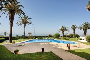 Ein Poolbereich mit freiem Blick auf das Meer, umgeben von Palmen und Liegestühlen.