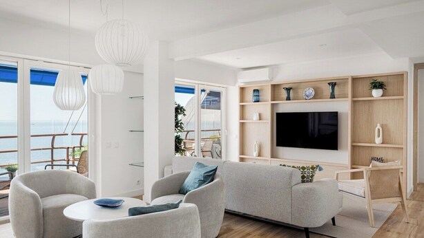 A modern living room with a large TV, comfortable seating, and a view of the sea. - Varandas do Mar - Estoril Atlantic Views (Cascais)