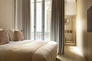 A hotel room with a bed, curtains, a view of the outside, and a small kitchenette. - Luxurious suite - AC- 2P- Madeleine/Saint Honore (Paris)
