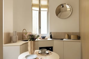 A modern kitchen with a dining area, a round mirror, and a window with blinds. - Luxurious suite - AC- 2P- Madeleine/Saint Honore (Paris)