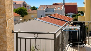 Una terraza en la azotea con barandilla de metal, un pequeño jardín y vistas a edificios vecinos.