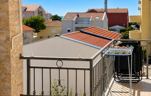 Eine Dachterrasse mit Metallgeländer, einem kleinen Gartenbereich und Blick auf angrenzende Gebäude.