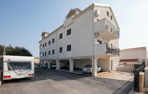 Ein mehrstöckiges Gebäude mit Tiefgarage, einem Bus und einem Auto vor der Fassade.