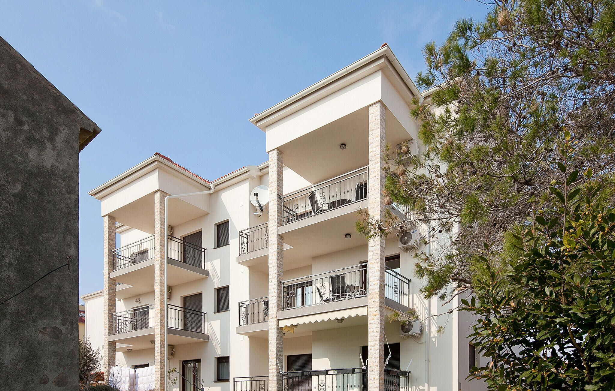 Un edificio residencial de varios pisos con balcones, unidades de aire acondicionado y un árbol en primer plano.