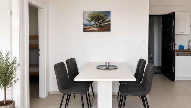 Un comedor con una mesa blanca y cuatro sillas, un cuadro en la pared y una planta en maceta.
