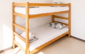 Een houten stapelbed met witte lakens en een kussen met een patroon.