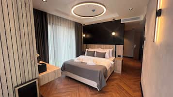 Una habitación de hotel moderna con una cama grande, mesitas de noche, televisión empotrada y suelo de madera.