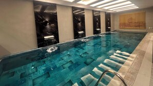 A modern indoor swimming pool with a clear water surface, a metal ladder, and a series of recessed lighting panels on the ceiling. - Vela Blu Suites (Trabzon)