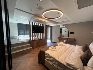 A modern hotel room with a large bed, a TV, a mirror, and a bathroom with a bathtub. - Vela Blu Suites (Trabzon)