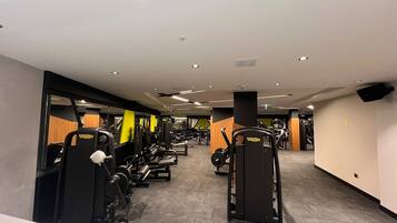 Un gimnasio con diversas máquinas de ejercicio, piso de baldosas e iluminación empotrada en el techo.