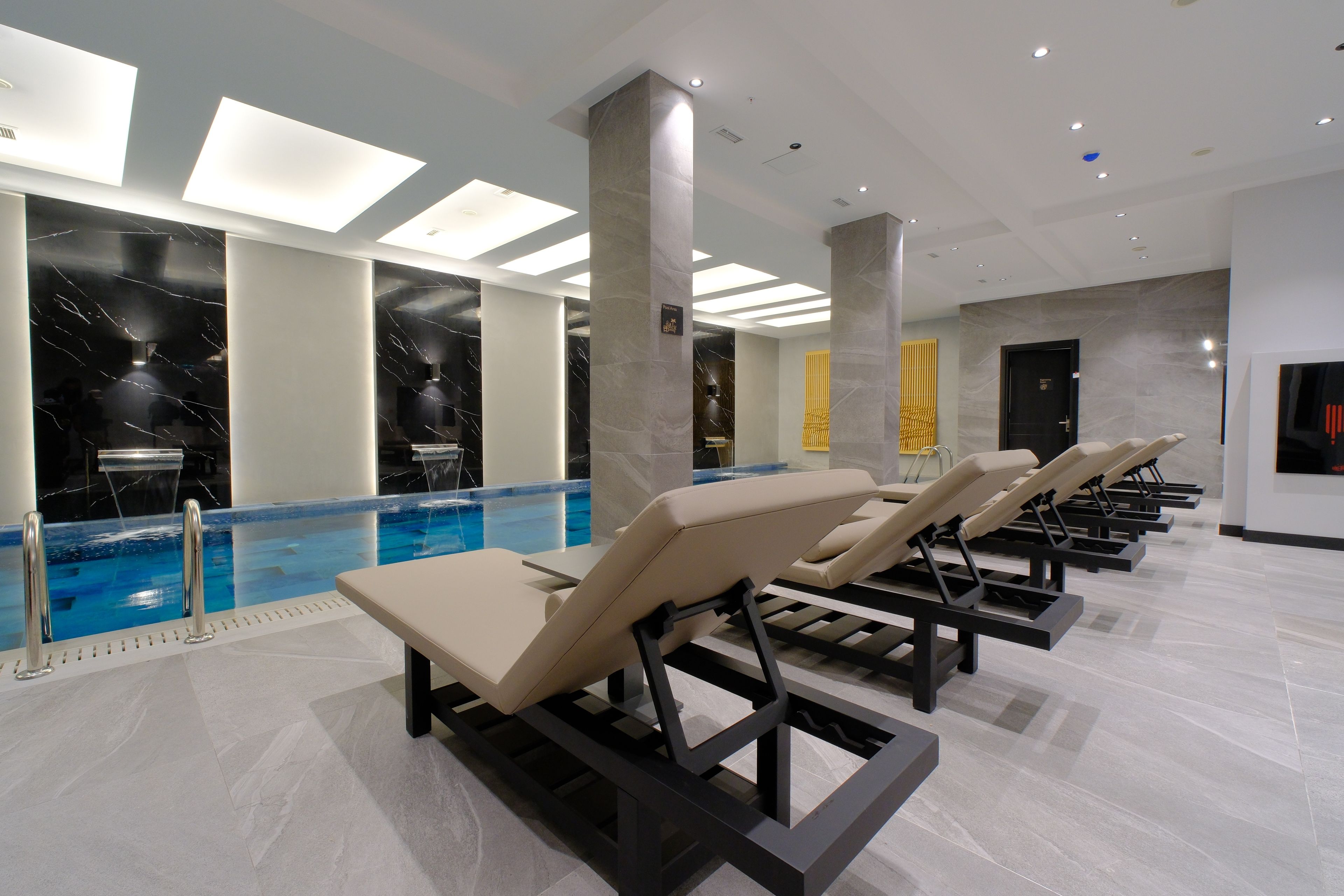 A modern indoor pool area with lounge chairs, a clear pool, and a ceiling with recessed lighting.