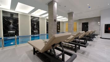 Un espace piscine intérieur moderne, doté de chaises longues, d’une piscine à eau claire et d’un plafond équipé d’un système d’éclairage encastré.