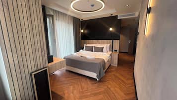 Una habitación de hotel moderna con una cama grande, suelo de madera e iluminación empotrada en el techo.