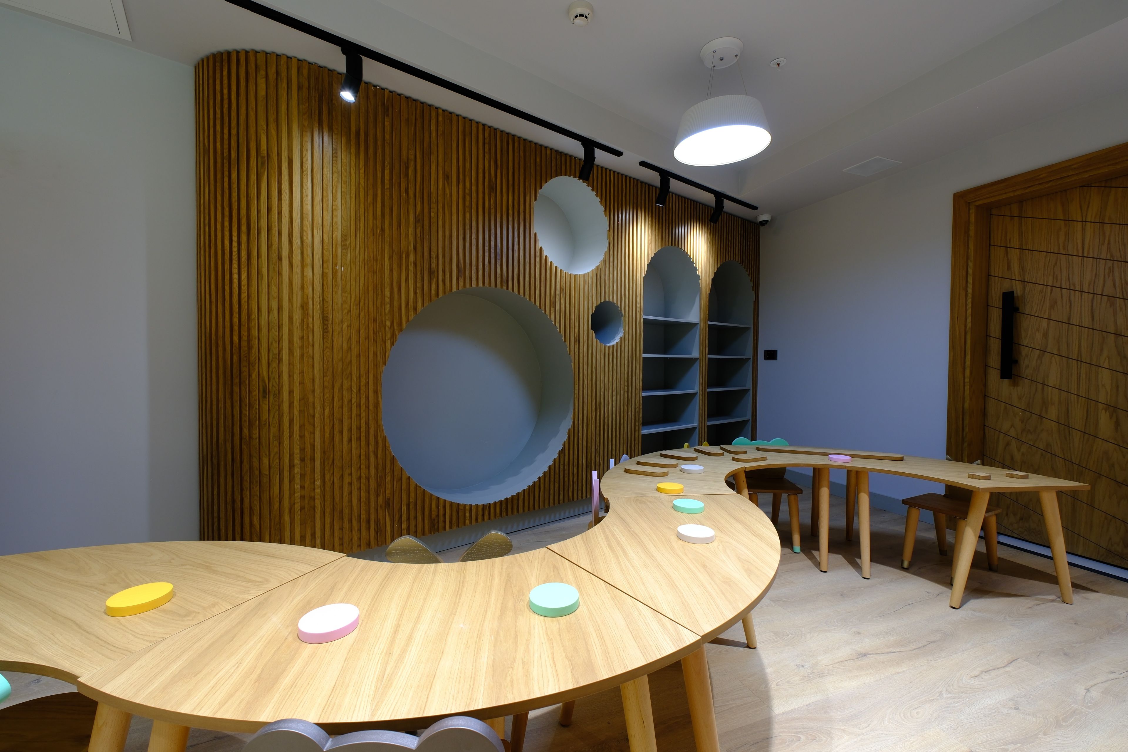 Una habitación con una mesa redonda de madera, una estantería y una pared de madera con recortes circulares.