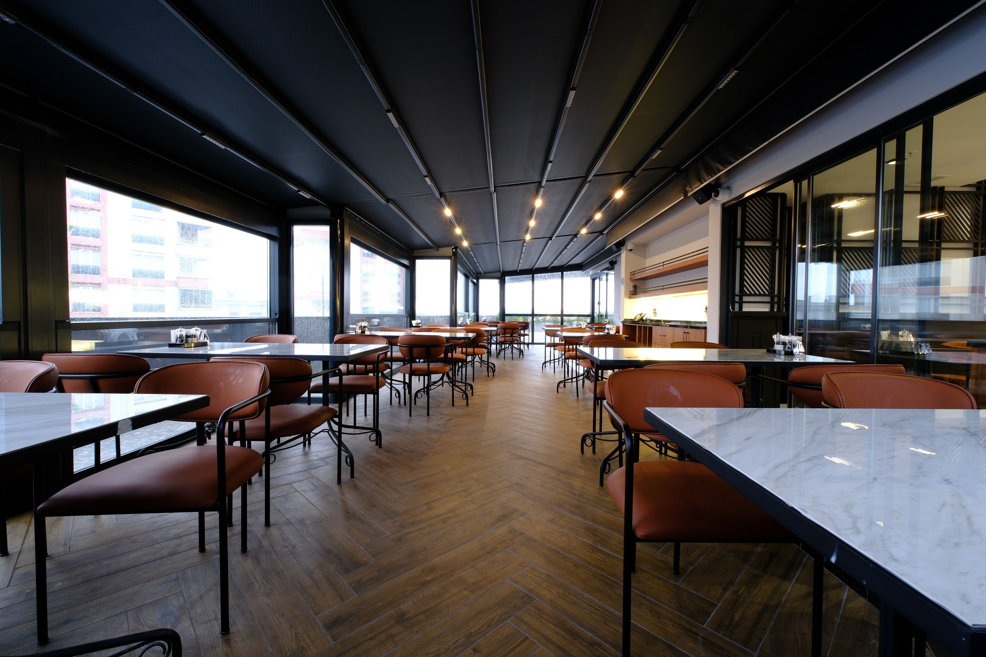 A spacious indoor dining area with multiple tables and chairs, large windows, and a modern ceiling design.