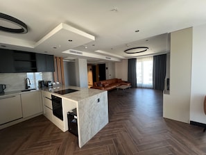 A modern kitchen with a central island, dark wood flooring, and a living area with a leather sofa. - Vela Blu Suites (Trabzon)