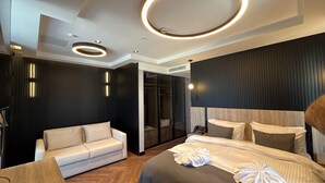 A modern hotel room with a bed, a sofa, a walk-in closet, and a circular ceiling light fixture. - Vela Blu Suites (Trabzon)