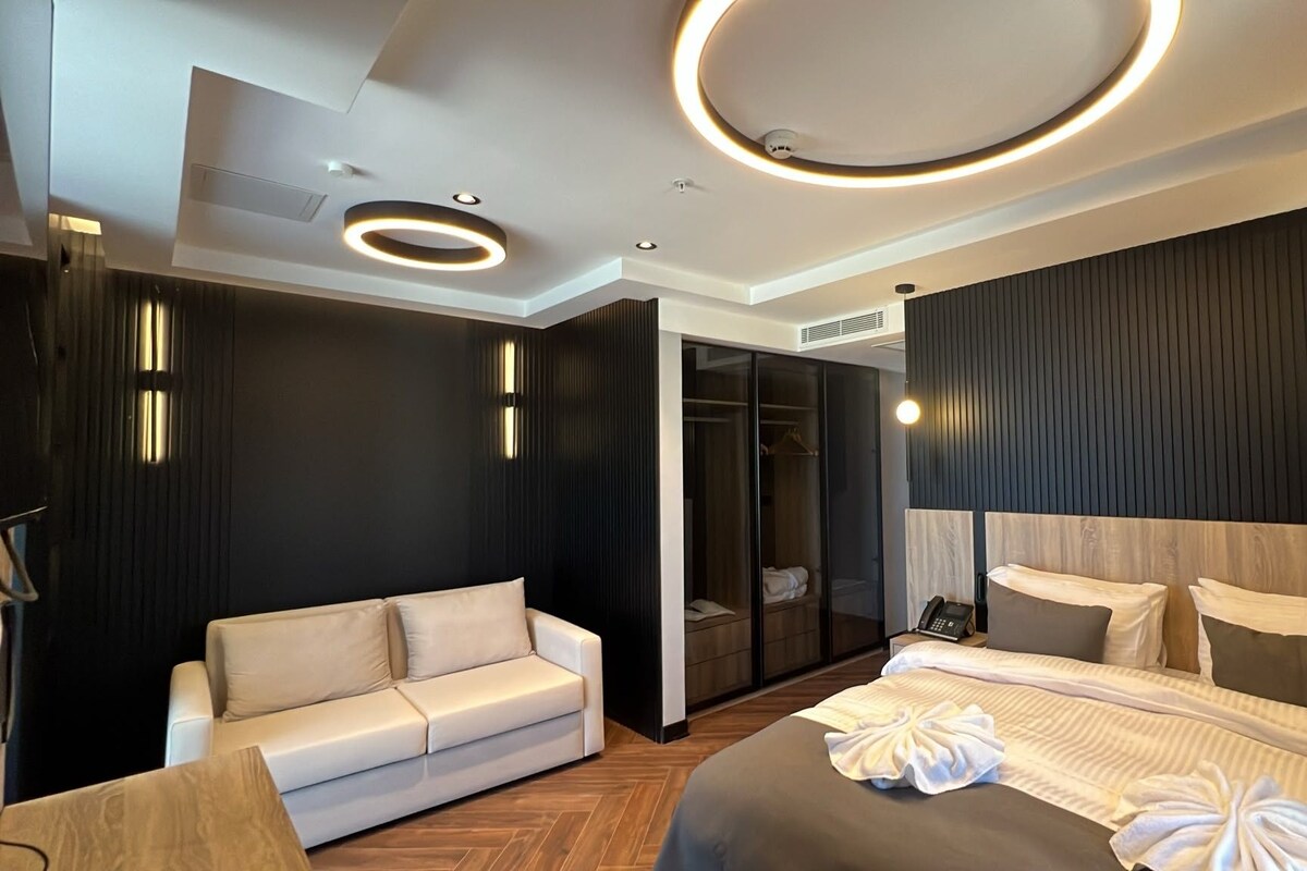 Una habitación de hotel moderna con cama, sofá, vestidor y una lámpara de techo circular.