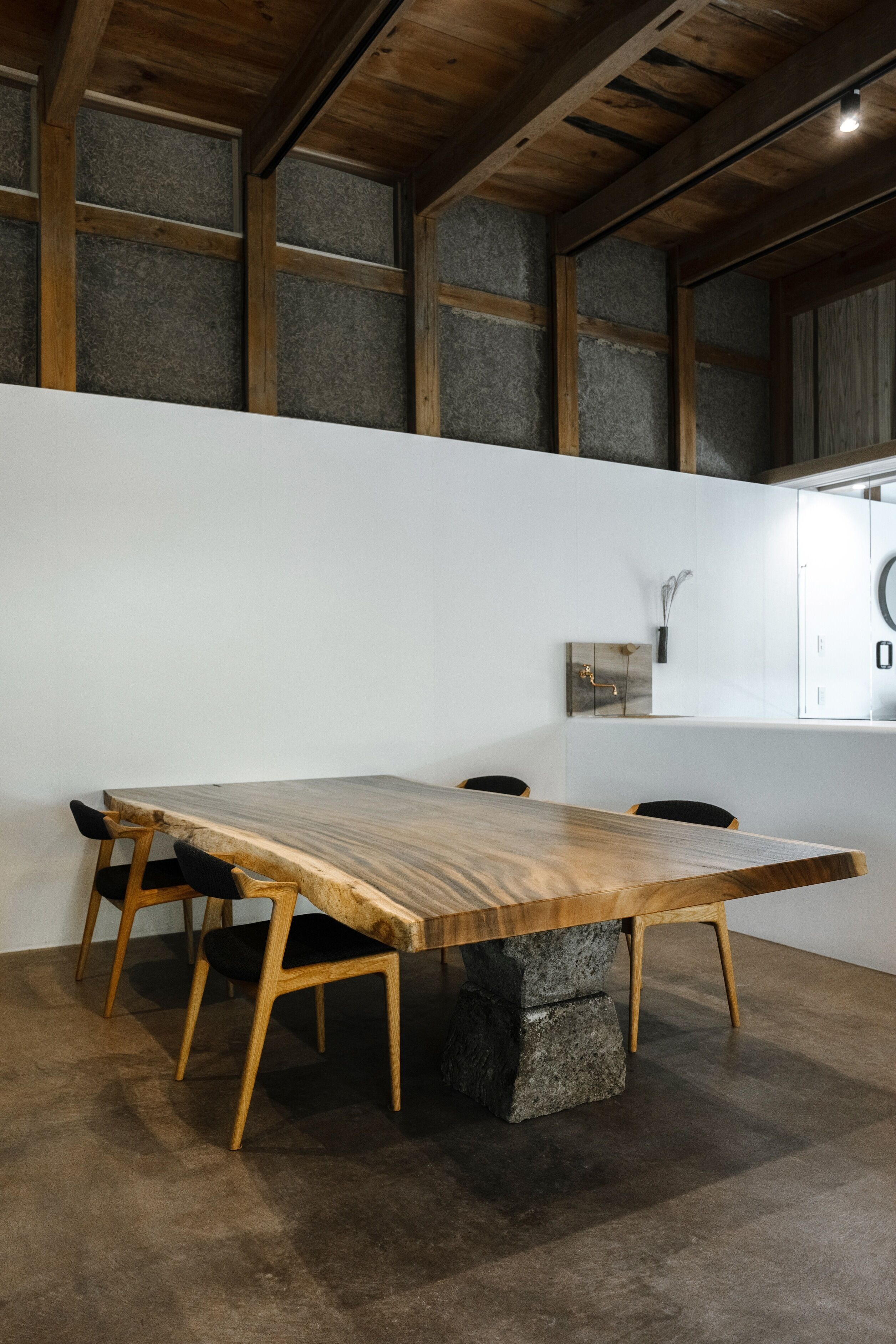 Un'area pranzo moderna con un tavolo e sedie in legno, zoccolo in pietra e vista su soffitto e pareti.