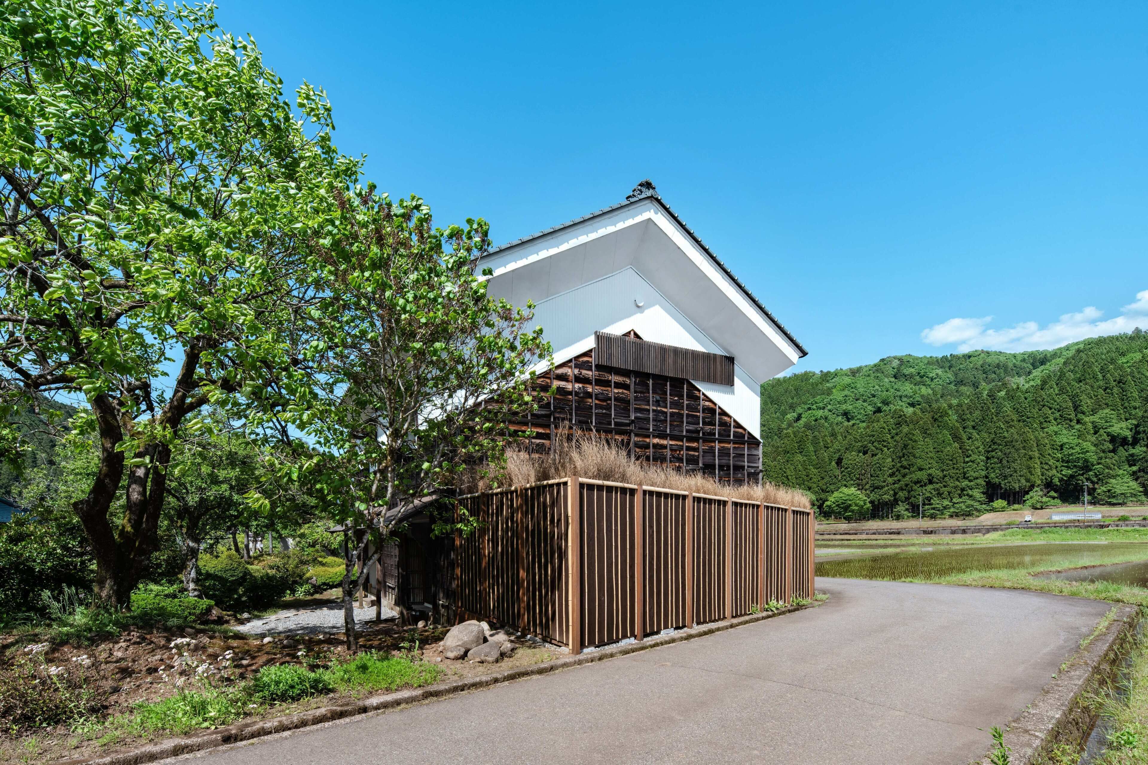A modern building with a sloped roof, surrounded by lush greenery and a clear sky.