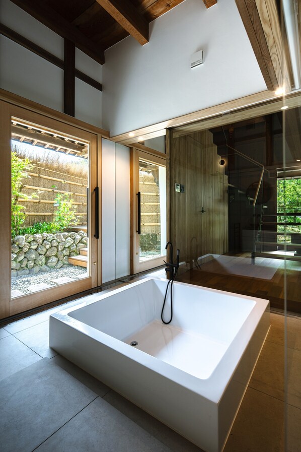A modern bathroom with a large bathtub, wooden beams, and a view of the outdoors.