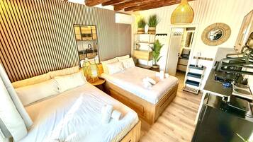 A modern hotel room with a large bed, a small desk, a mirror, and a kitchen area.