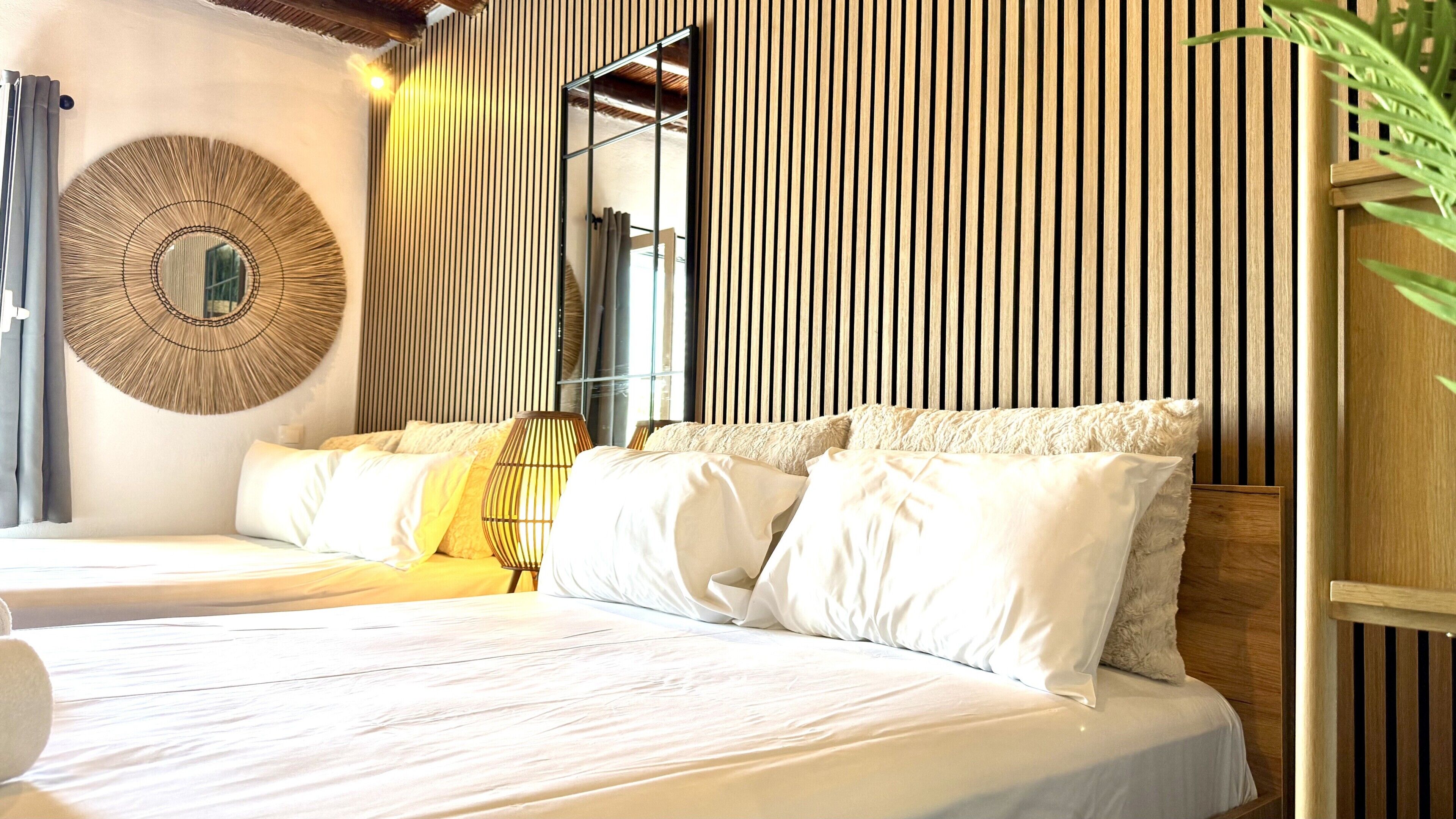 Ein Bett mit weißen Leinentüchern, ein runder Wandspiegel und eine Wand aus Holzlatten.