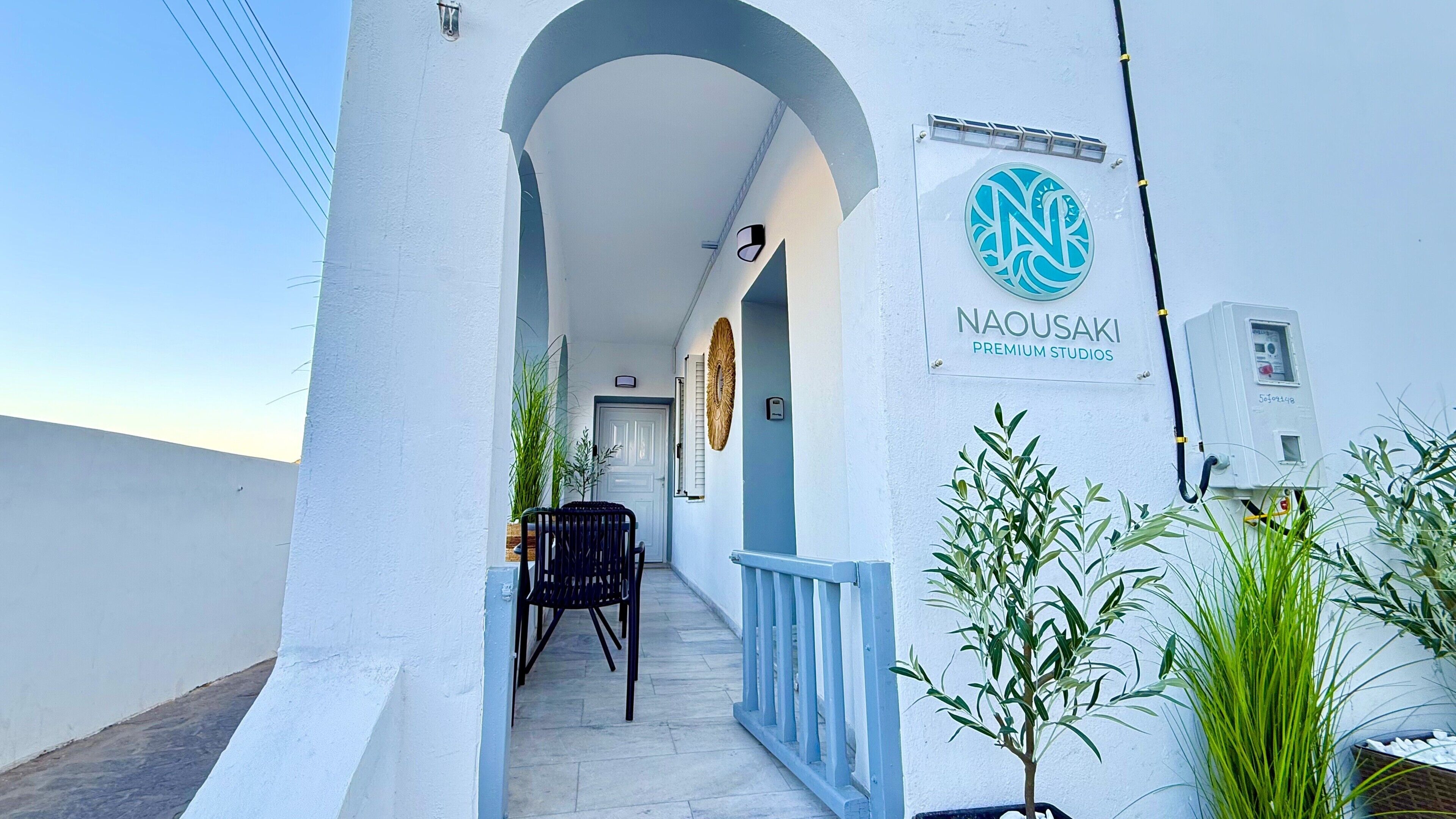 A white building with a sign for 'NAOUSAKI PREMIUM STUDIOS' and a clear sky.