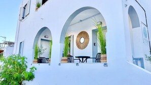 Un edificio blanco con tres ventanas arqueadas, un espejo redondo y plantas en macetas.