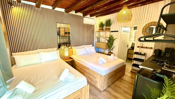 Una habitación de hotel con dos camas, una kitchenette, un espejo y una lámpara colgante.