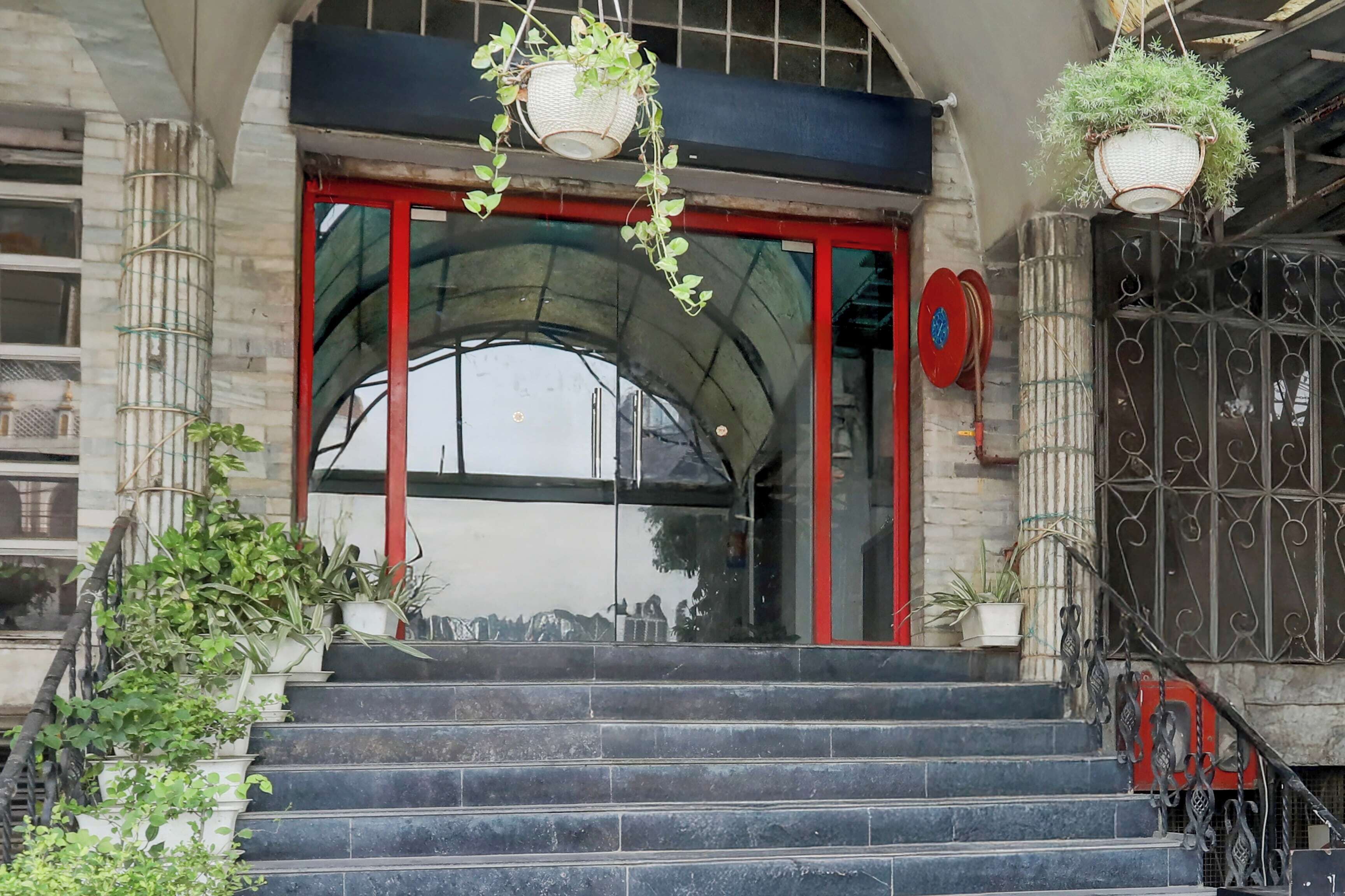 A building entrance with a red door, a staircase, and hanging plants.
