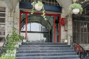 Entrada de un edificio con puerta roja, una escalera y plantas colgantes.
