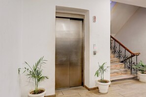 En elevator, en trappe med smedejernsrækværk og potteplanter.