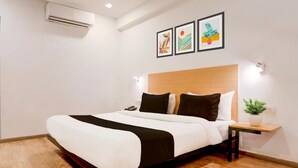 A hotel room with a bed, bedside table, wall-mounted air conditioner, and framed artwork. - Townhouse Prayagraj Near Railway Station Formerly Santosh Palace (Prayagraj)