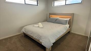 A bedroom with a bed, ceiling fan, two windows, and carpeted floor.