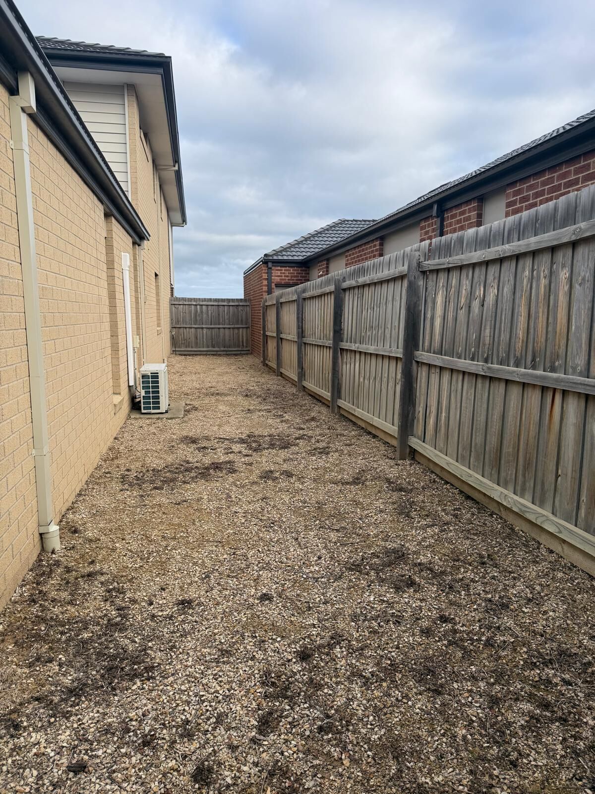 A backyard with a wooden fence, a brick building, and a gravel ground.