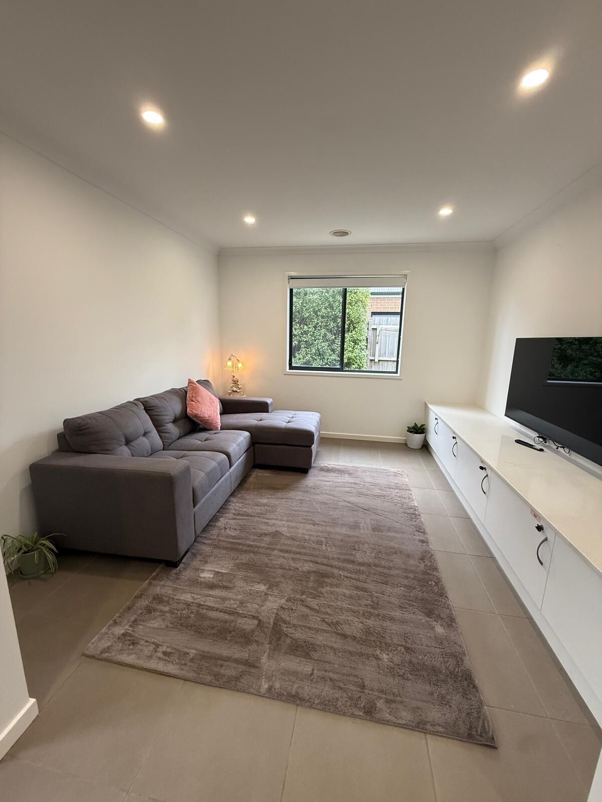 A modern living room with a sectional sofa, a flat-screen TV, and a large window.