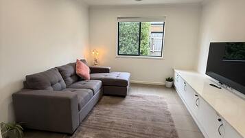 A modern living room with a sectional sofa, a flat-screen TV, and a large window.