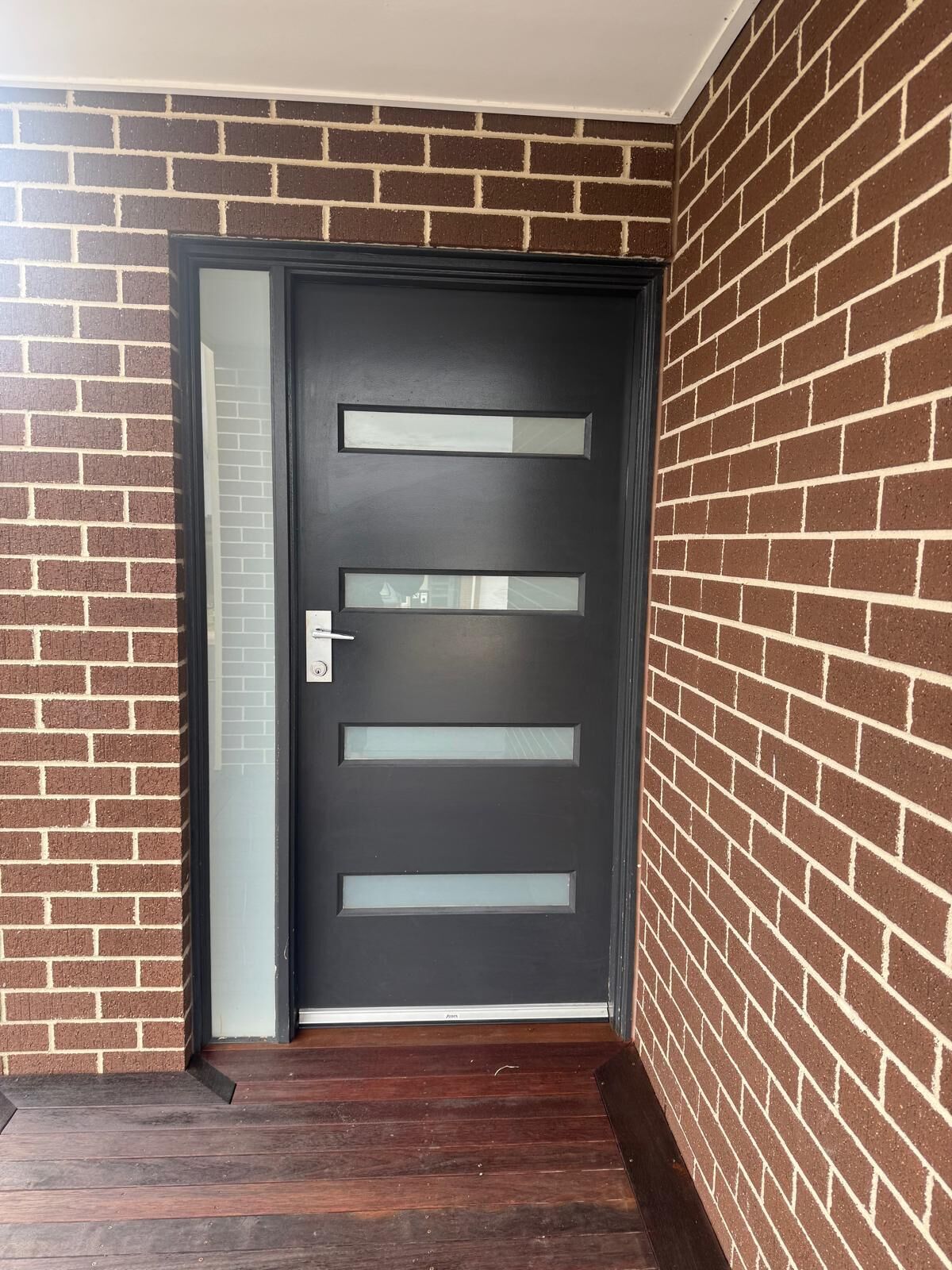 A dark-colored door with frosted glass panels, set in a brick wall with a wooden floor.
