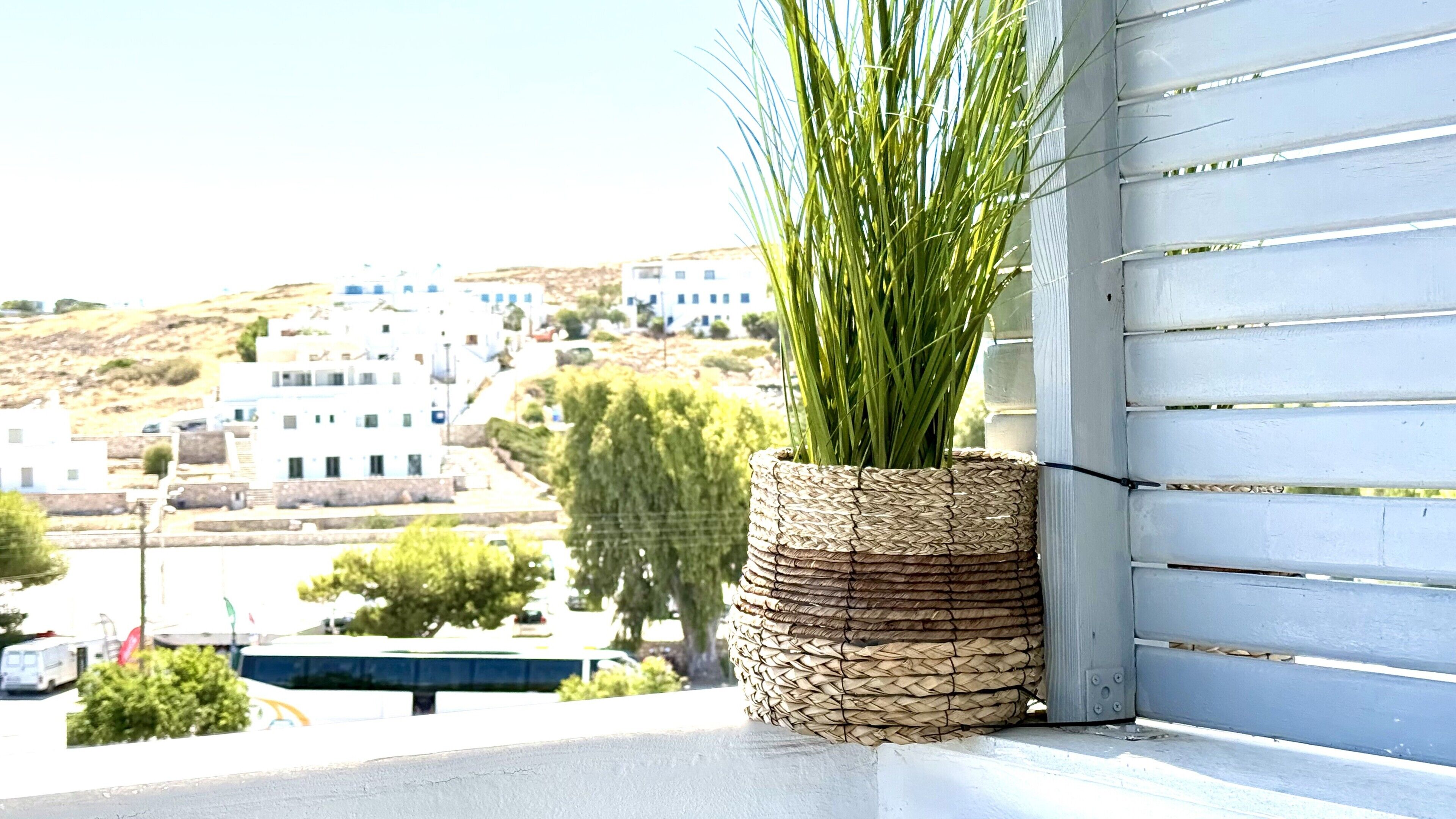 A corner view of a building with a woven basket containing green plants, overlooking a coastal town with white buildings and a clear sky.