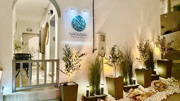 A hotel entrance with a sign for Naousaki Premium Studios, a staircase, and potted plants.