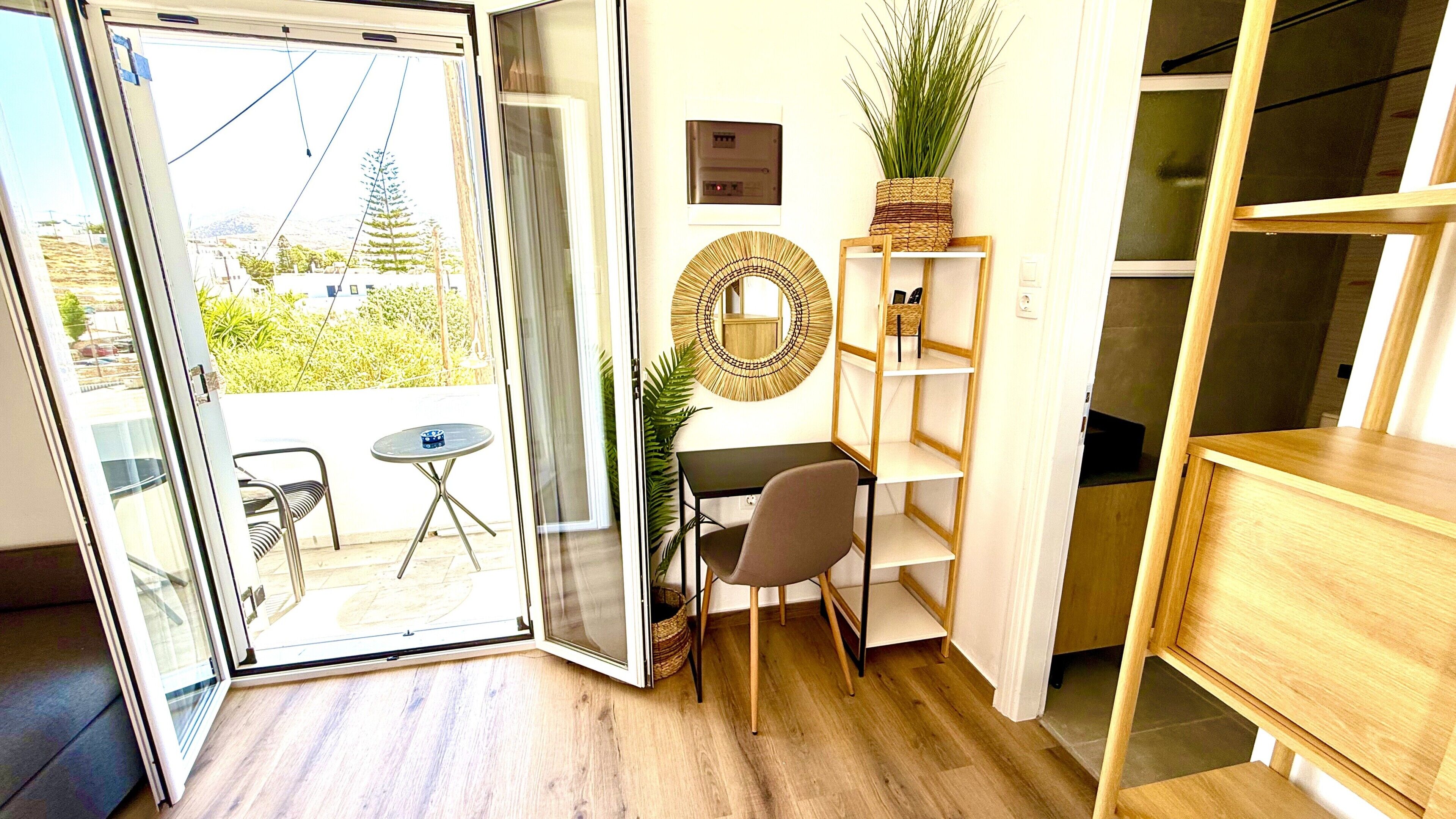 Una habitación con puerta corrediza de vidrio que da a un espacio exterior, una pequeña mesa redonda, una silla, un estante en la pared con una planta y un mueble de madera.