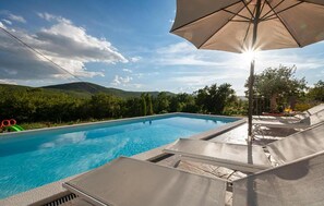 A swimming pool with lounge chairs and an umbrella, surrounded by greenery and hills. - Nice home in Cista velika (Cista velika)