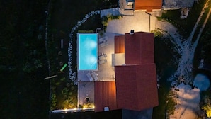 Vista aérea de uma propriedade com piscina, alpendre coberto e um edifício com telhado vermelho.