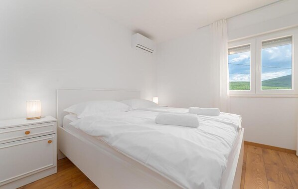 Een witte slaapkamer met een bed, nachtkastjes, een raam met uitzicht en een airconditioning.