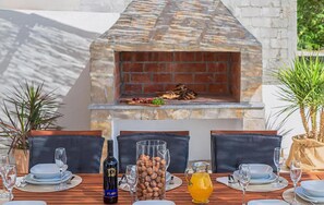 An outdoor dining area with a brick oven, seating, and a table set with plates, glasses, and a bottle. - Nice home in Cista velika (Cista velika)