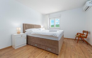 A bedroom with a bed, a nightstand, a chair, a window, and an air conditioning unit. - Nice home in Cista velika (Cista velika)